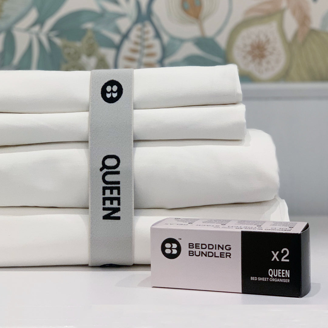 Stack of white queen-sized bed sheets with a bedding bundler packaging on a floral-patterned background.