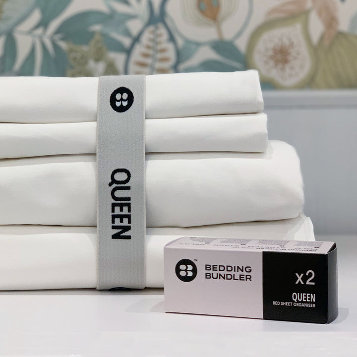 Stack of white queen-sized bed sheets with a bedding bundler packaging on a floral-patterned background.