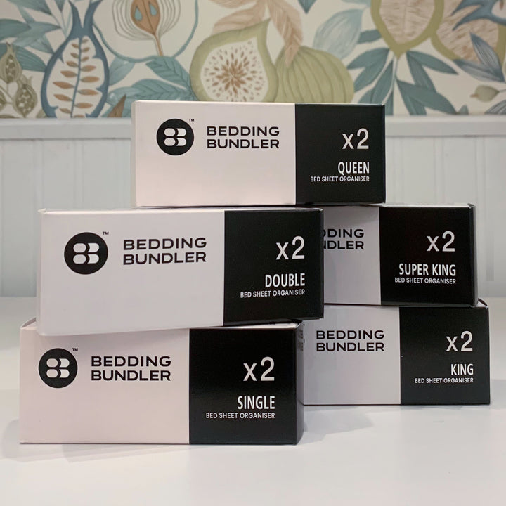 Stack of Bedding Bundler boxes with various bed size options on a floral wallpaper background.