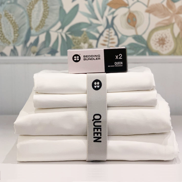 Stack of white bedding with a 'Bedding Bundler' box on a floral-patterned wall background