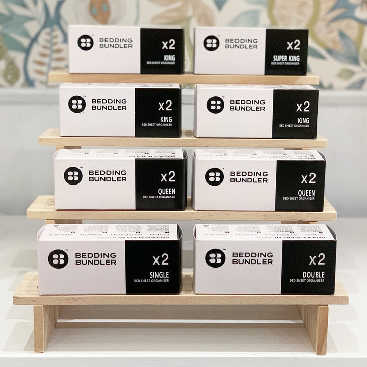 Stack of 'Bedding Bundler' boxes on a wooden stand with decorative background