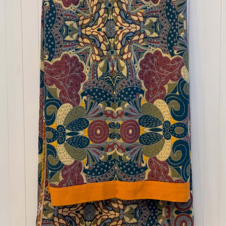 The cool-toned reverse of the Daphne blanket displayed folded on a rail. Rich hues of navy, plum, olive, and ochre create an intricate, symmetrical design.