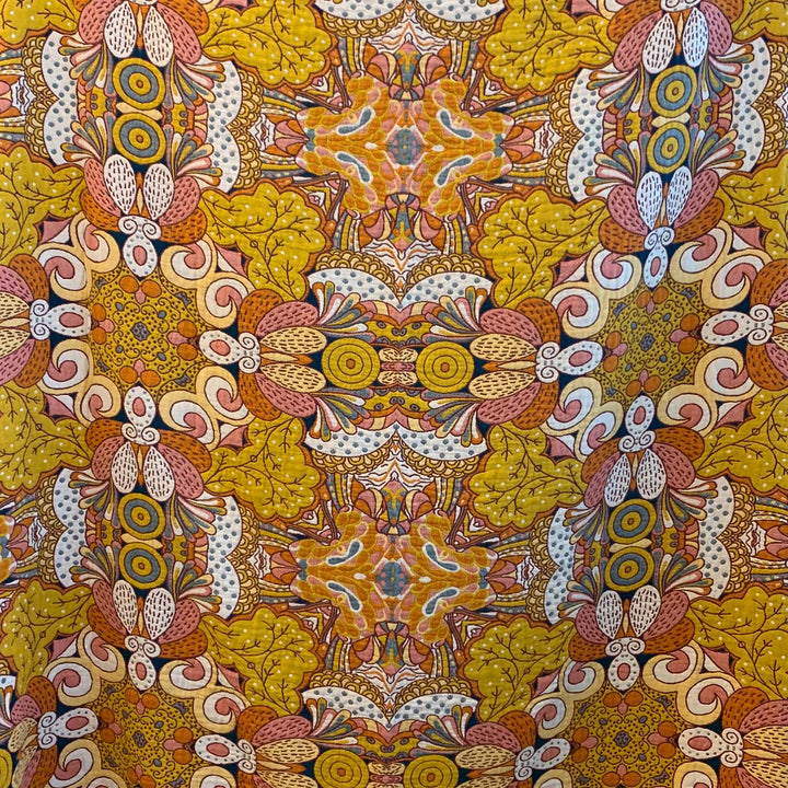 A detailed fabric close-up of the warm side of the Daphne blanket. Features bold graphic florals, golden leaves, and swirling patterns in a mirrored kaleidoscope layout.