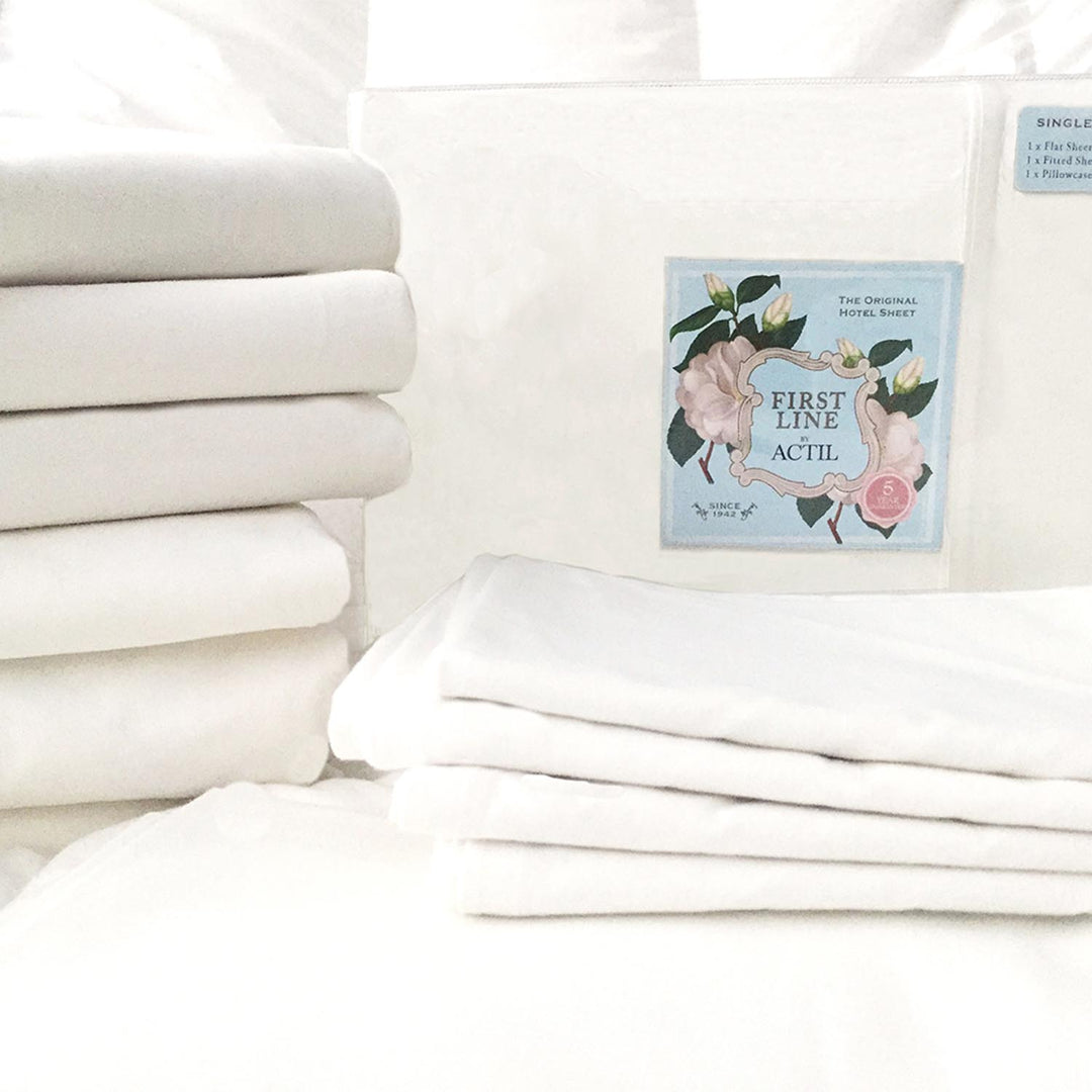 Close-up of packaged Actil First Line sheet set stacked on folded sheets, highlighting premium hotel-quality cotton