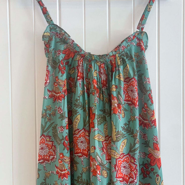 Belinda cotton nightie in teal blue with floral print, gathered neckline and thin straps, shown hanging on white timber wall