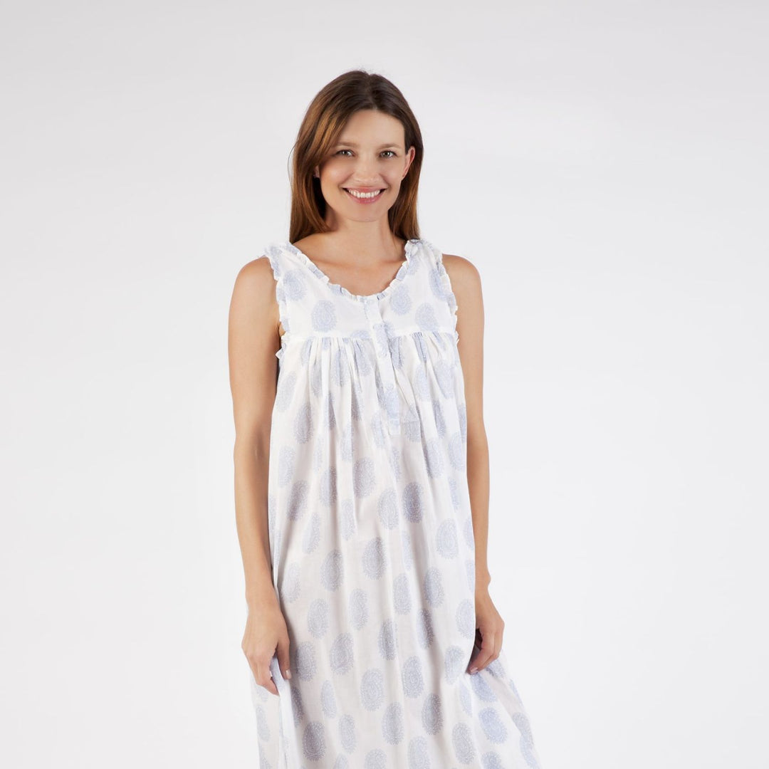 Woman wearing the Clara cotton nightie in white with soft blue paisley print, smiling and facing front against a white background