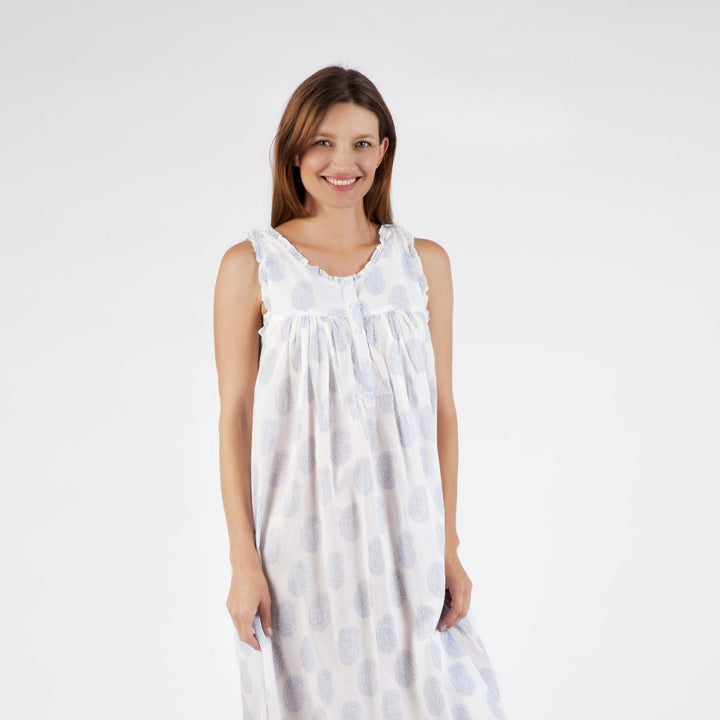 Woman wearing the Clara cotton nightie in white with soft blue paisley print, smiling and facing front against a white background