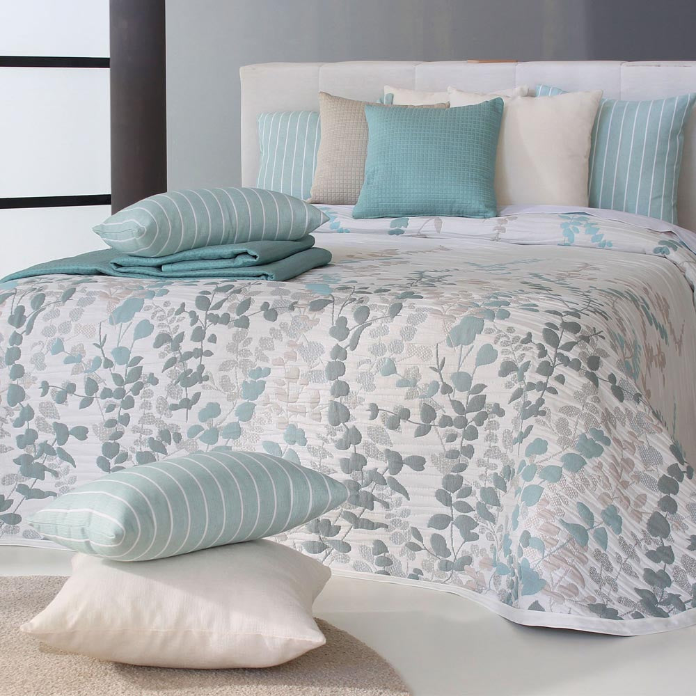 White bedspread with soft eucalyptus leaf pattern in blue and taupe, styled with coordinating teal and neutral cushions.