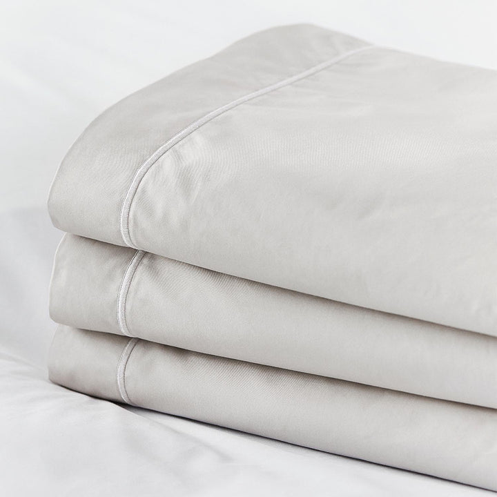 Stack of taupe Egyptian cotton fitted top sheets with white piping