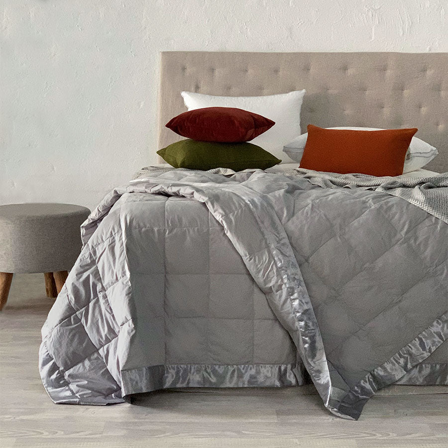 Grey feather down blanket styled on a bed with white pillows and autumn-toned cushions