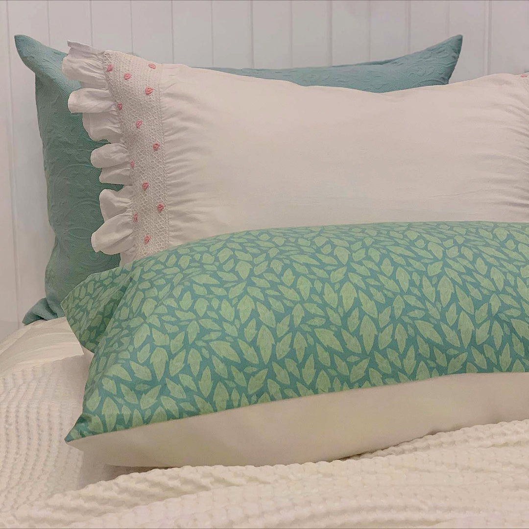 A RE/Loved Actil Hollybush pillowcase styled on a bed with white textured bedding and soft green and white cushions.