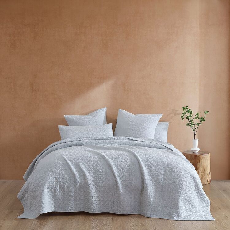 A light grey coverlet on a bed, with geometric stitching, displayed in a bedroom setting.
