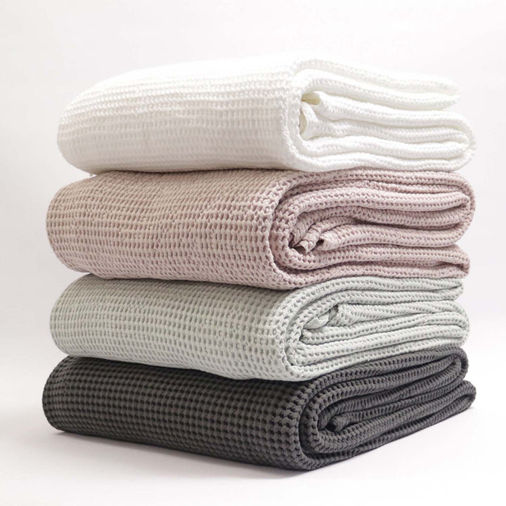 A stack of folded waffle texture blankets in various colors including white, beige, gray, and blue.