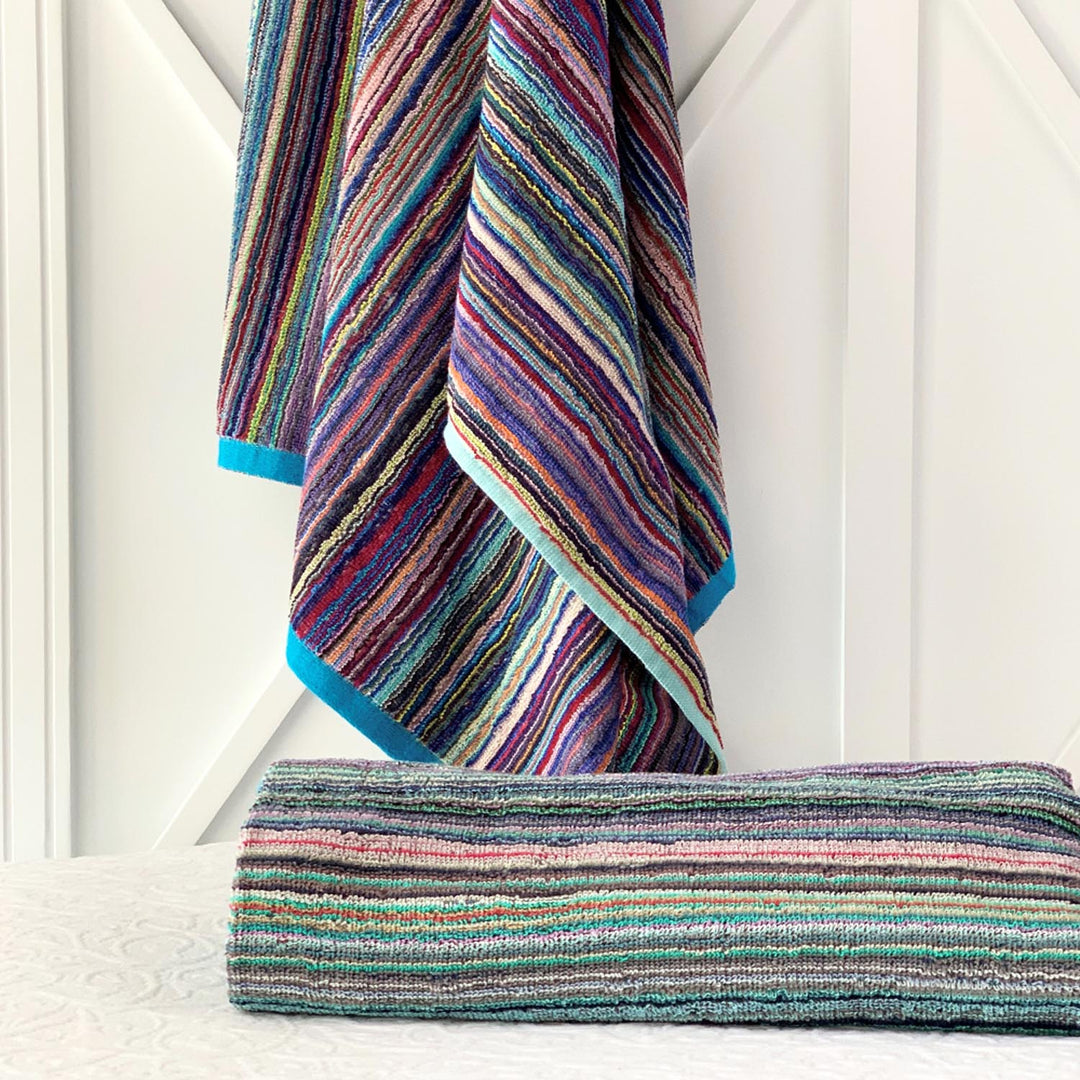 A multicolored striped towel hanging on a white door, with a rolled up towel showing the same colorful pattern.