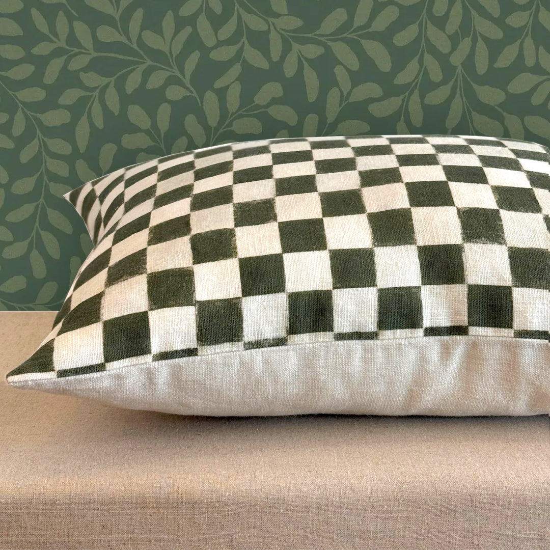Checkered pillow on a beige surface with a green leafy patterned wall in the background