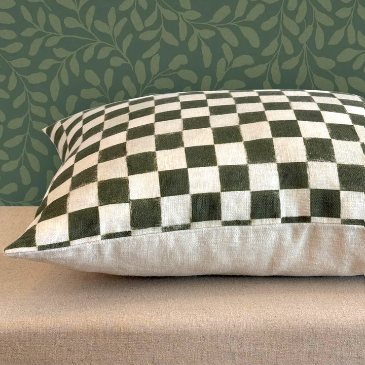 Checkered pillow on a beige surface with a green leafy patterned wall in the background