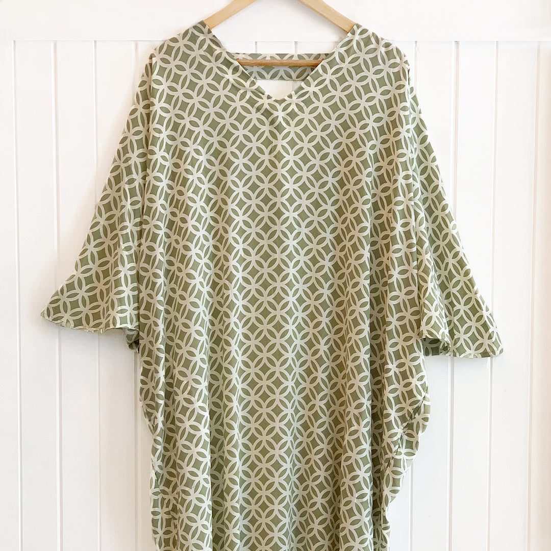 Green and white patterned dress on a wooden hanger against a white wooden panel background