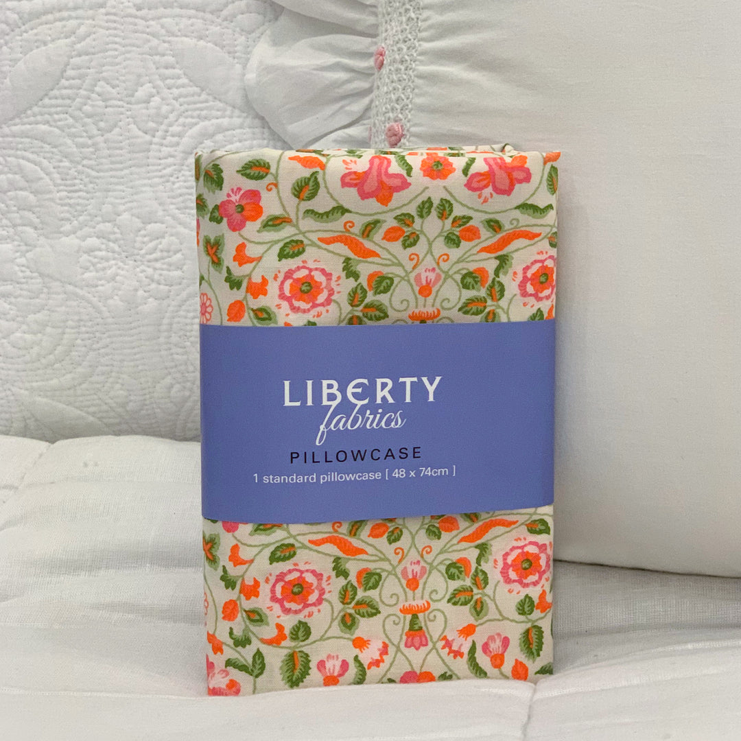 Packaged Liberty Fabrics pillowcase with floral design on a bed background