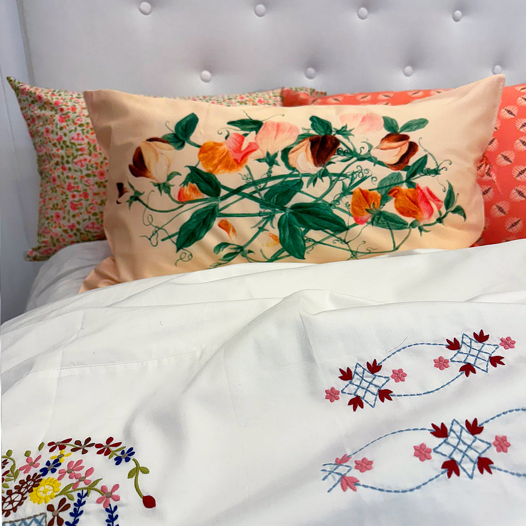 Embroidered floral patterns on pillows and a blanket against a gray headboard.