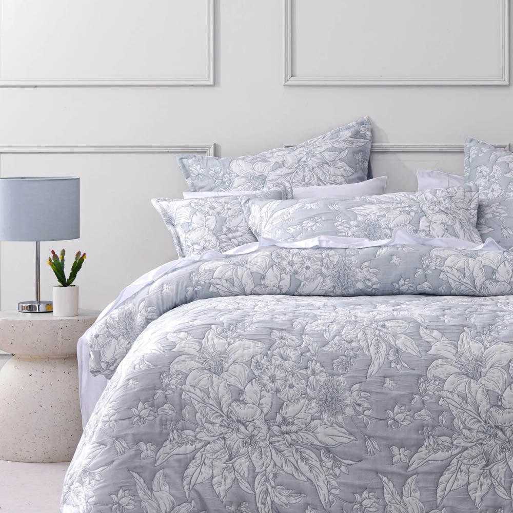 Floral patterned bedding set on a bed in a bedroom with a lamp and plant.