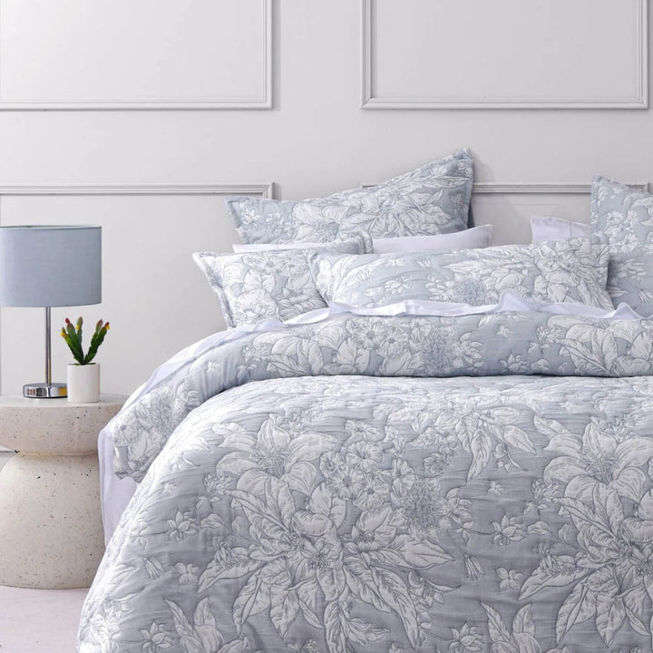 Floral patterned bedding set on a bed in a bedroom with a lamp and plant.