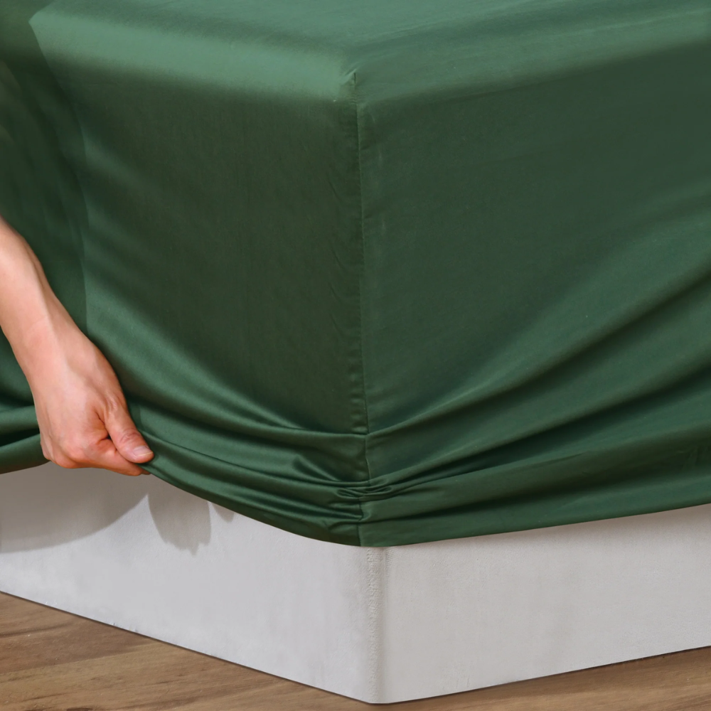 Hand pulling Bianca Forest Green fitted sheet over mattress corner, demonstrating deep fit and stretch.