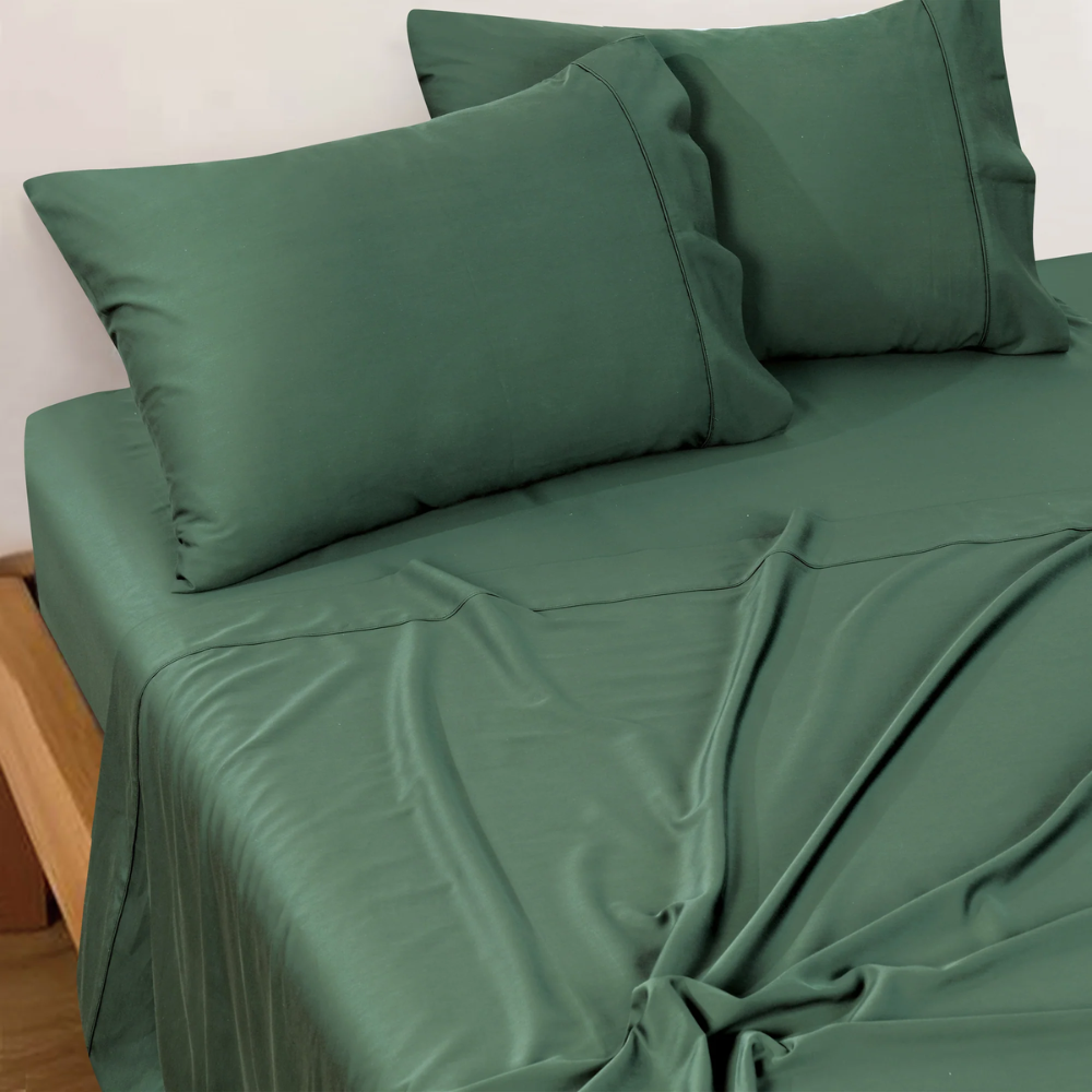 Bianca Forest Green sheet set styled on a bed, featuring flat sheet, fitted sheet, and two matching pillowcases.