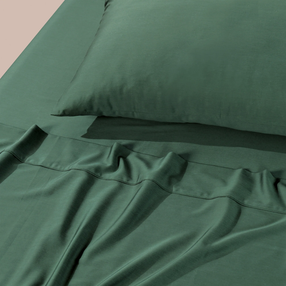 Flat lay of Bianca Forest Green sheet set with pillowcase, highlighting crisp stitching and deep green tone.