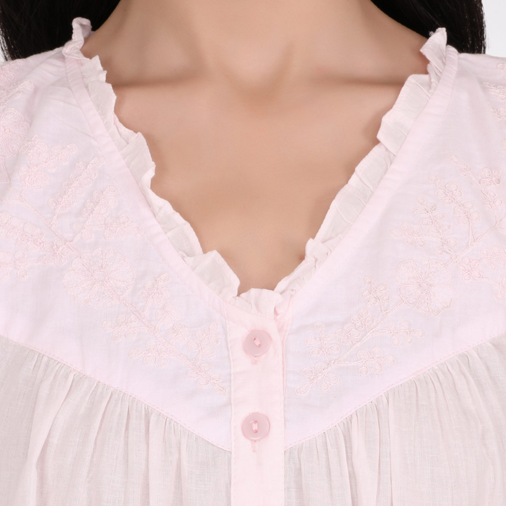 Close-up of a white lace-trimmed garment with pink buttons on a mannequin.
