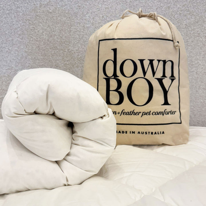White pet comforter and beige storage bag labeled 'down BOY' on a light gray background