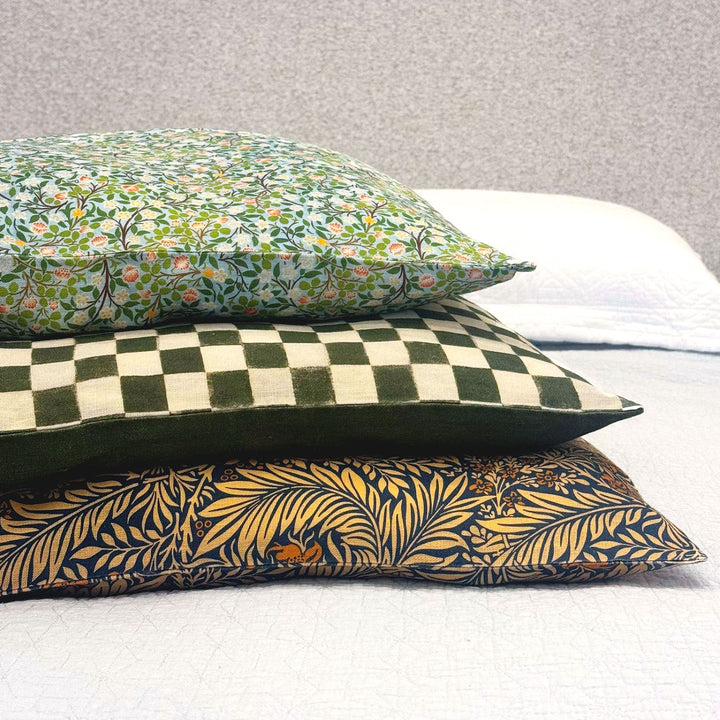 Three patterned pillows stacked on a bed with a neutral background