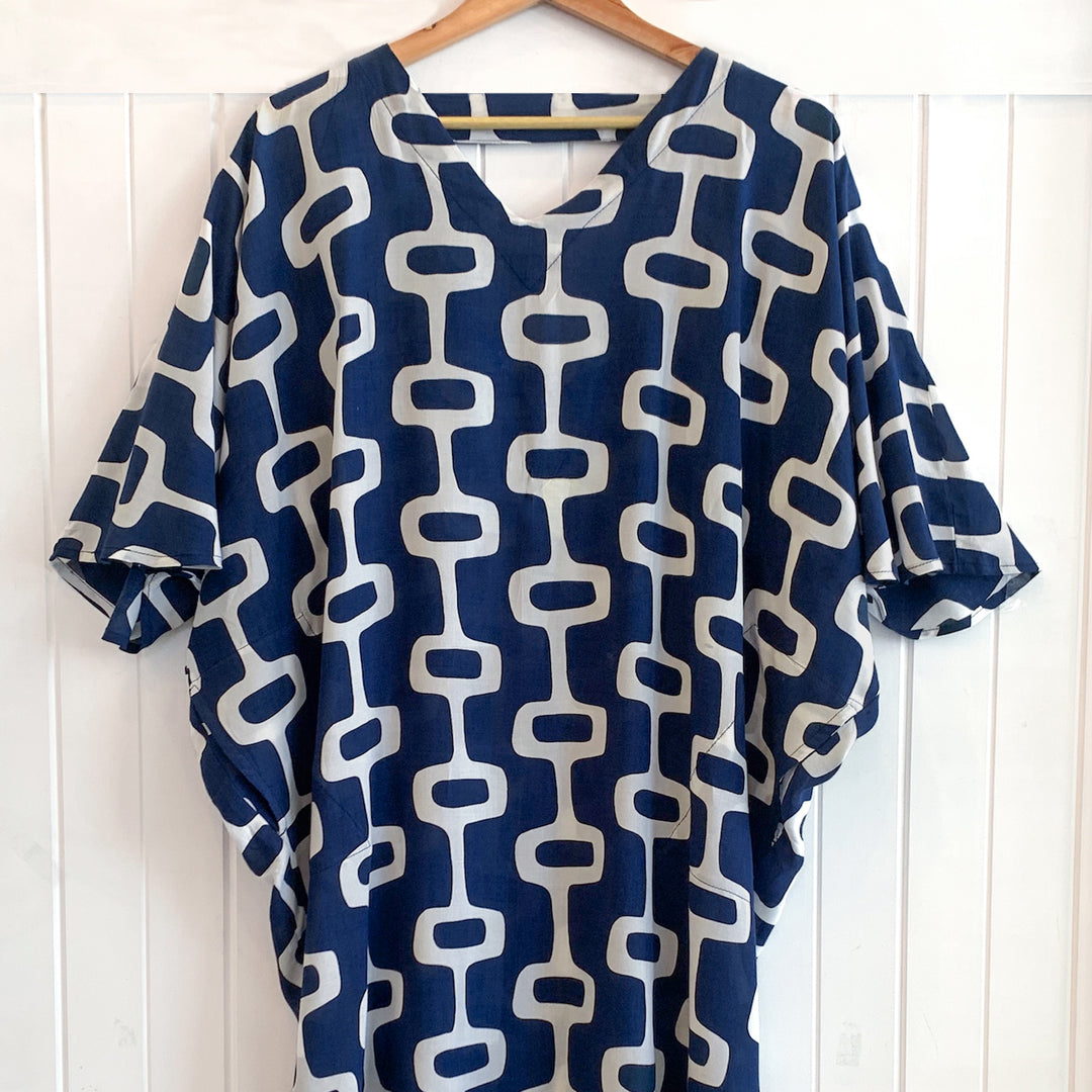 Blue and white patterned dress on a wooden hanger against a white wooden panel background