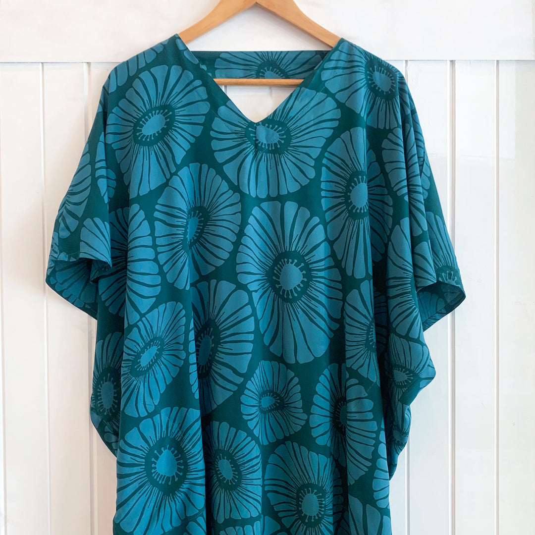 Teal floral patterned garment on a wooden hanger against a white wooden panel background