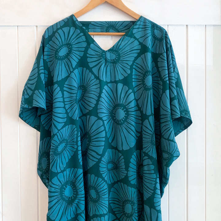 Teal floral patterned garment on a wooden hanger against a white wooden panel background