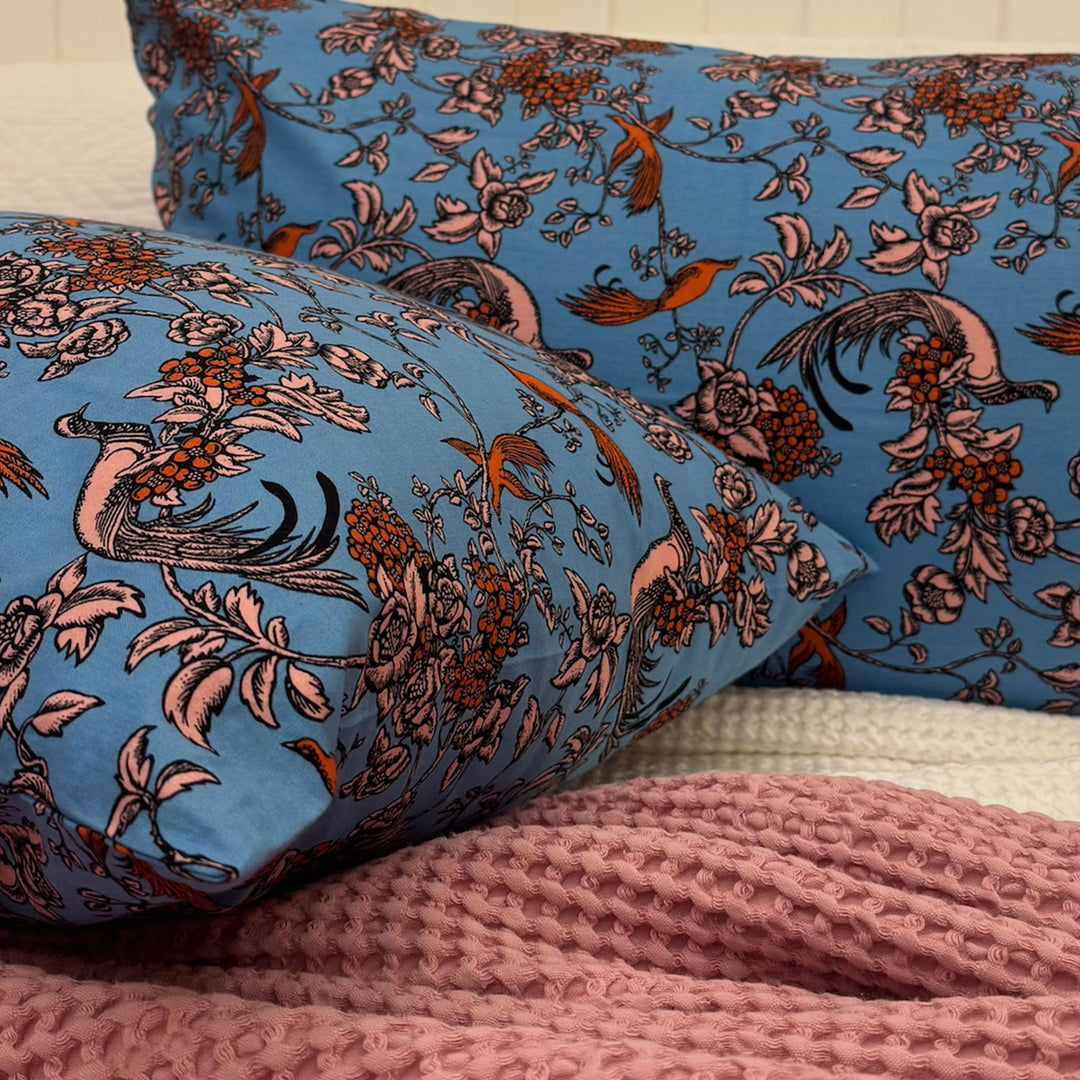 Floral patterned pillows on a bed with a pink textured blanket.