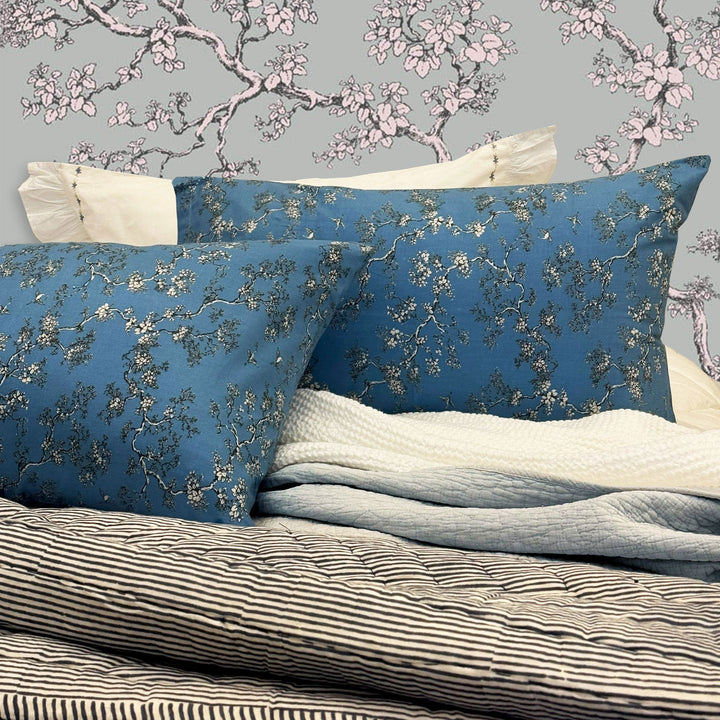 Blue floral-patterned pillowcases on a bed with cherry blossom wallpaper.