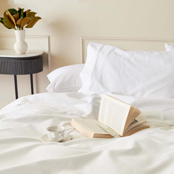 White Egyptian cotton bed sheets styled with an open book and tea on bed